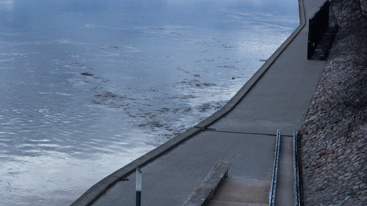 A serene view of a river promenade with cobblestone paving by the calm water's edge at dusk.