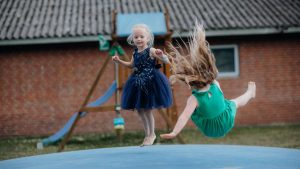 Two girls enjoy jumping on a trampoline outside. Fun and laughter in a playful setting.