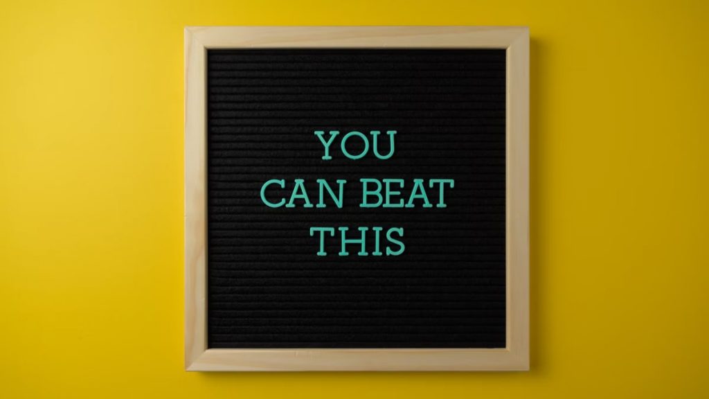 Black letter board with motivational phrase 'You Can Beat This' on vibrant yellow background.
